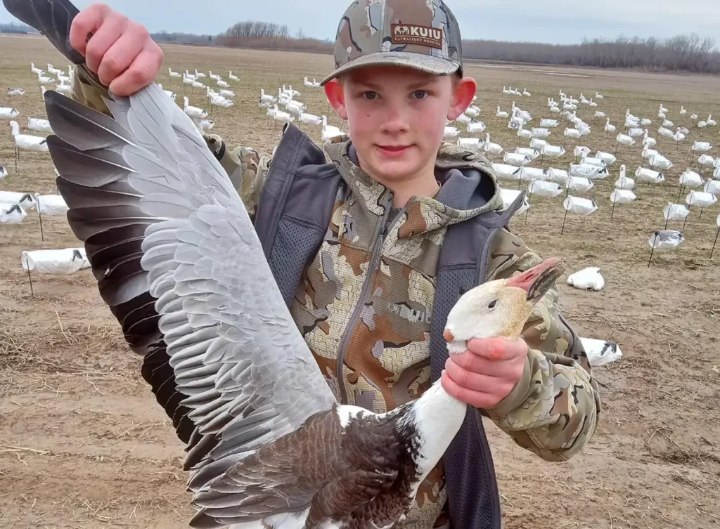 young boy holding up a snow goose he hunted - waterfowl hunting - arkansas and southern illinois