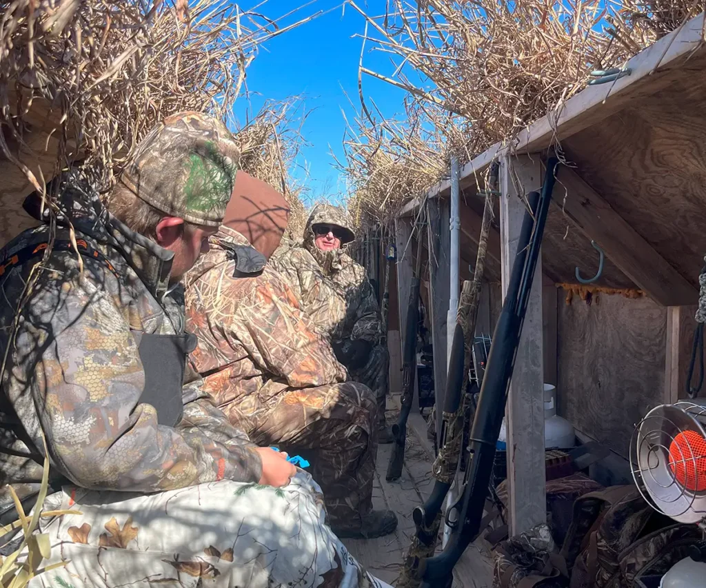 Hunters seated quietly in a camouflaged blind, patiently waiting for snow geese to arrive during a waterfowl hunt