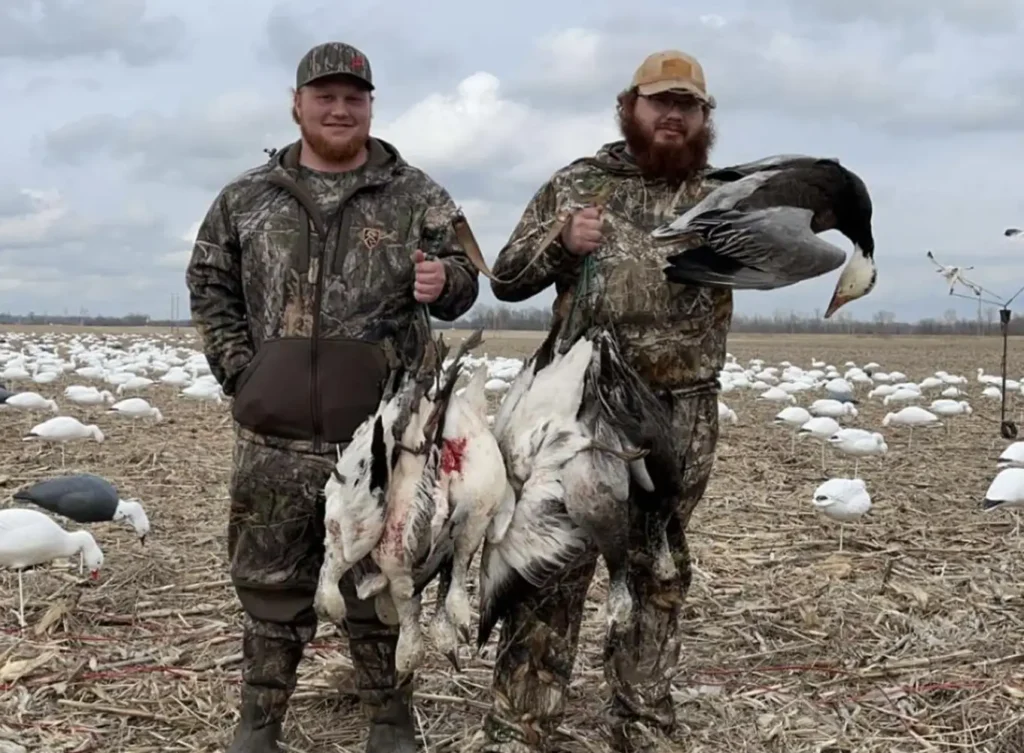 2 men wearing hunting gear holding up their waterfowl game in illinois